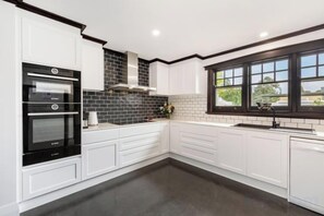 A kitchen with white cabinetry, a black oven, and a window with a view. - Whiterocks Tanunda Walk to Cafés Sleeps 8 Heritage (Tanunda)
