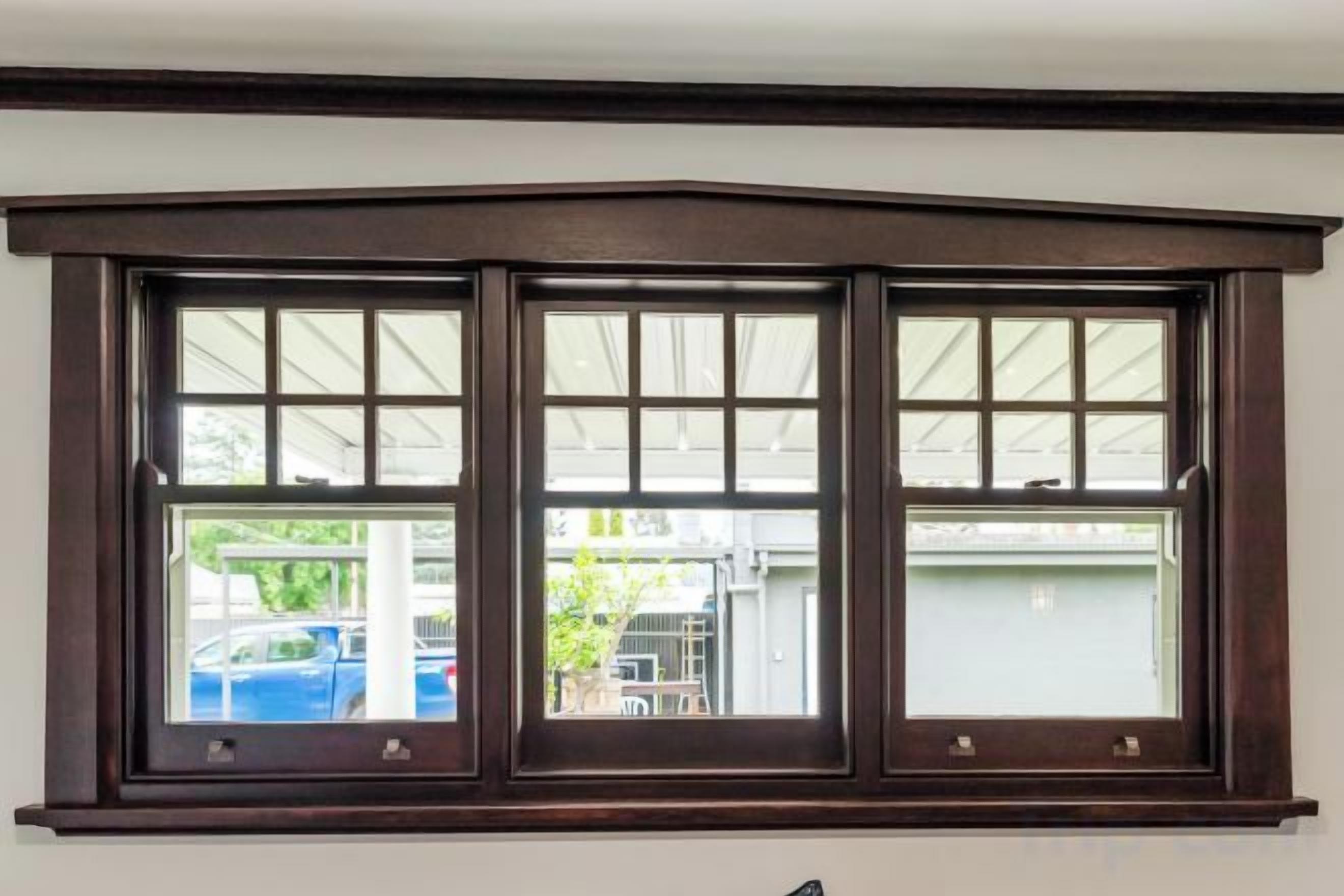 A bay window with three panes, a white wall, and a view of a garage with a car and a covered area.