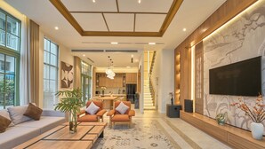 Uma sala de estar ampla com sofá, poltronas, mesa de centro e televisão na parede.