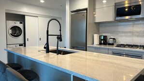 A modern kitchen with a built-in washer and dryer, a stainless steel refrigerator, and a gas stove. - Infinite blue (Vancouver)