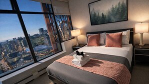 A hotel room with a large window, a bed with pillows, a bedside table with a lamp, and a painting on the wall. - Infinite blue (Vancouver)