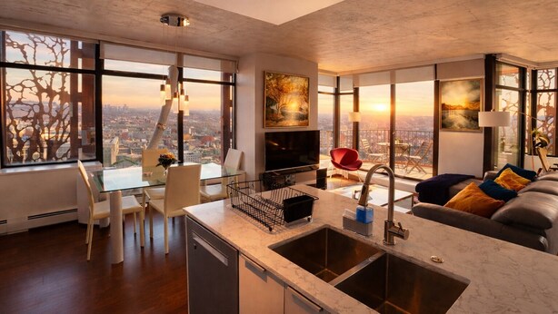 A modern living room with a kitchen, dining area, and large windows offering city views. - Infinite blue (Vancouver)