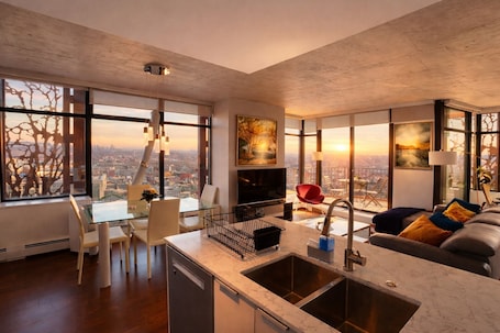 A modern living room with a kitchen, dining area, and large windows offering city views.. Infinite blue