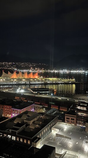 Paisagem urbana noturna com rio, edifícios iluminados e uma ponte com estruturas laranja características.