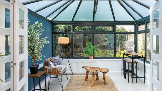 Ein Wintergarten mit Glasdach, einer Sitzecke inklusive Tisch und Stühlen, und Zimmerpflanzen.