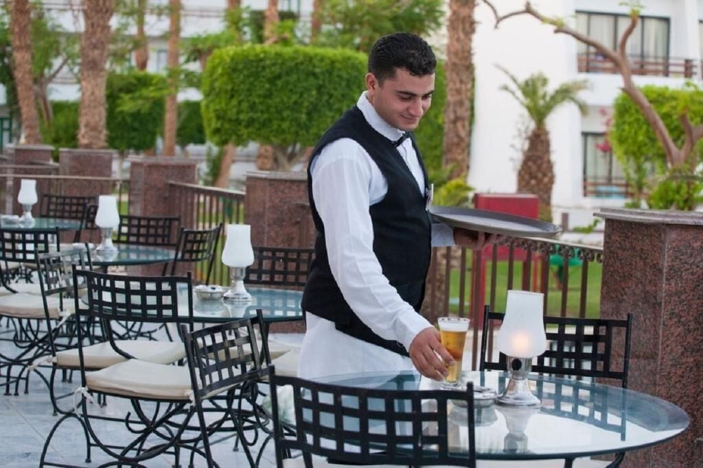 A waiter serving a drink at an outdoor table with chairs and a lamp.