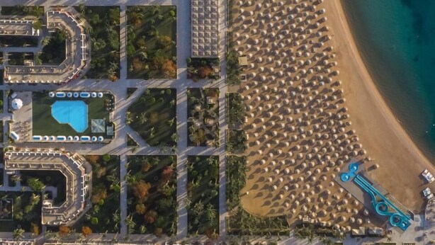 Vue aérienne d’une station balnéaire dotée d’une vaste plage, de plusieurs piscines et d’un port de plaisance.