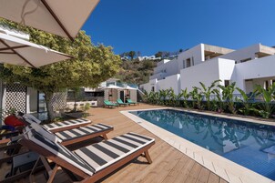Zona junto a la piscina con sillas de descanso, piscina y vista a una colina con edificios.