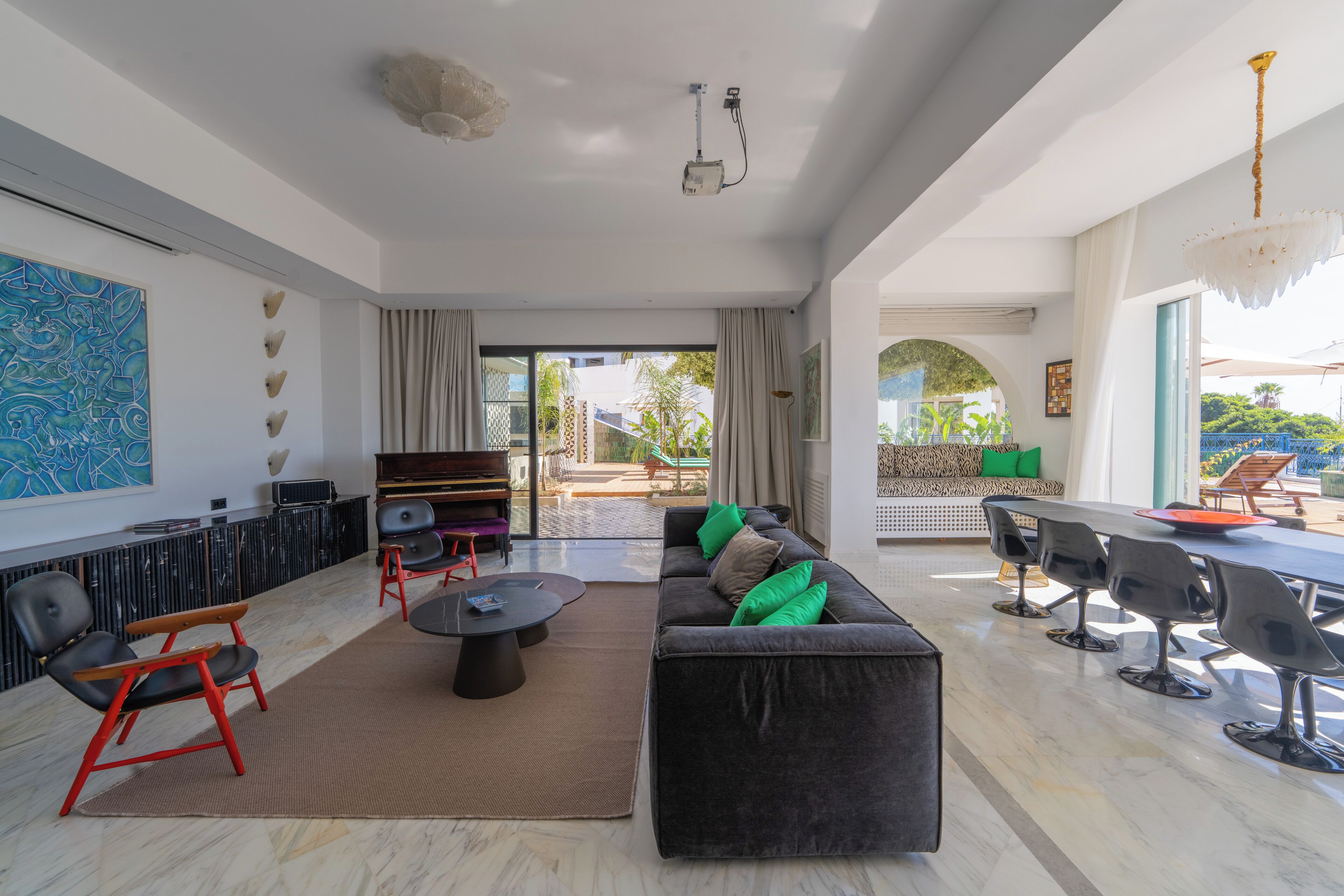 Un amplio salón con sofá, sillones, una mesa baja y una mesa de comedor con sillas. Una ventana grande ofrece vistas al exterior.