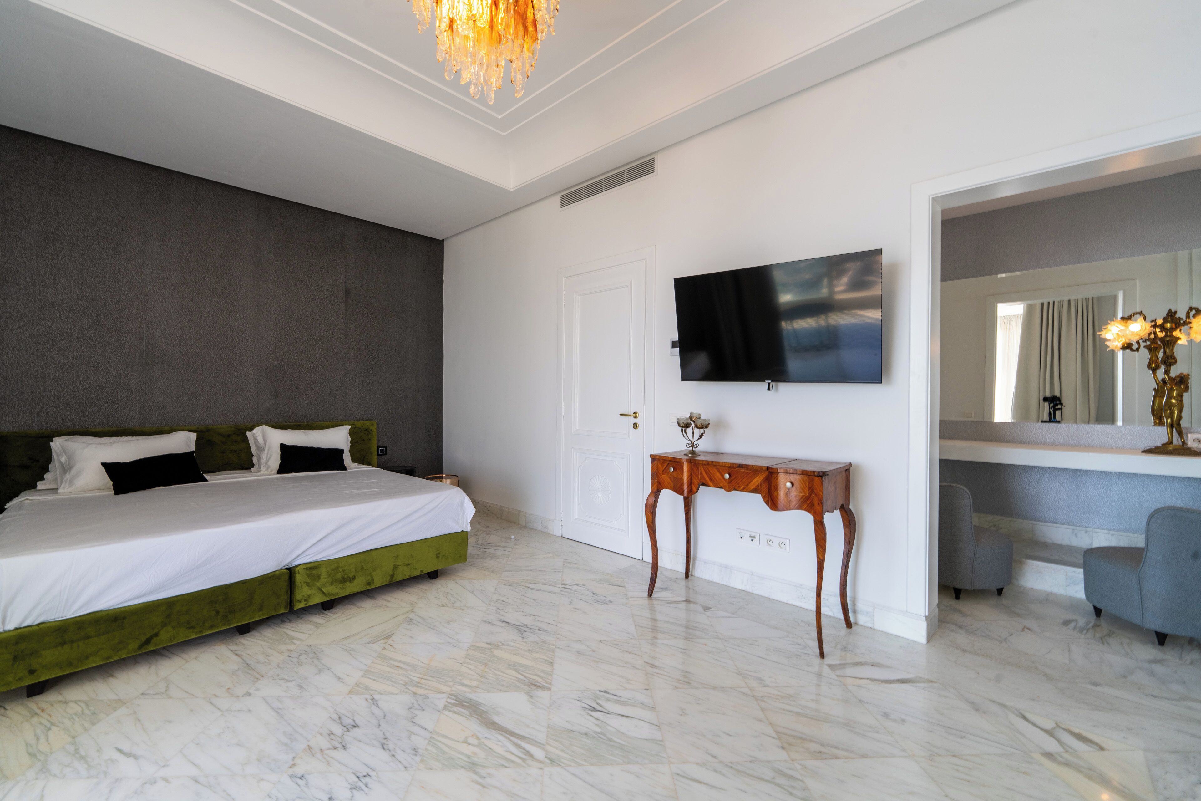 Quarto moderno com cama verde, televisão de tela plana, mesa de cabeceira de madeira e espelho.