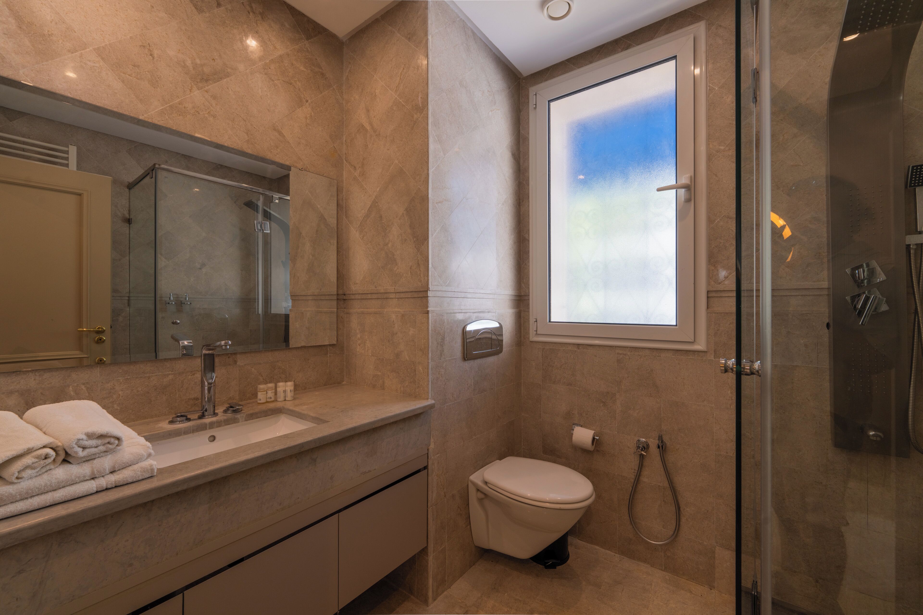 Un baño moderno con ducha envuelta en vidrio, un espejo grande, un lavamanos y un inodoro.