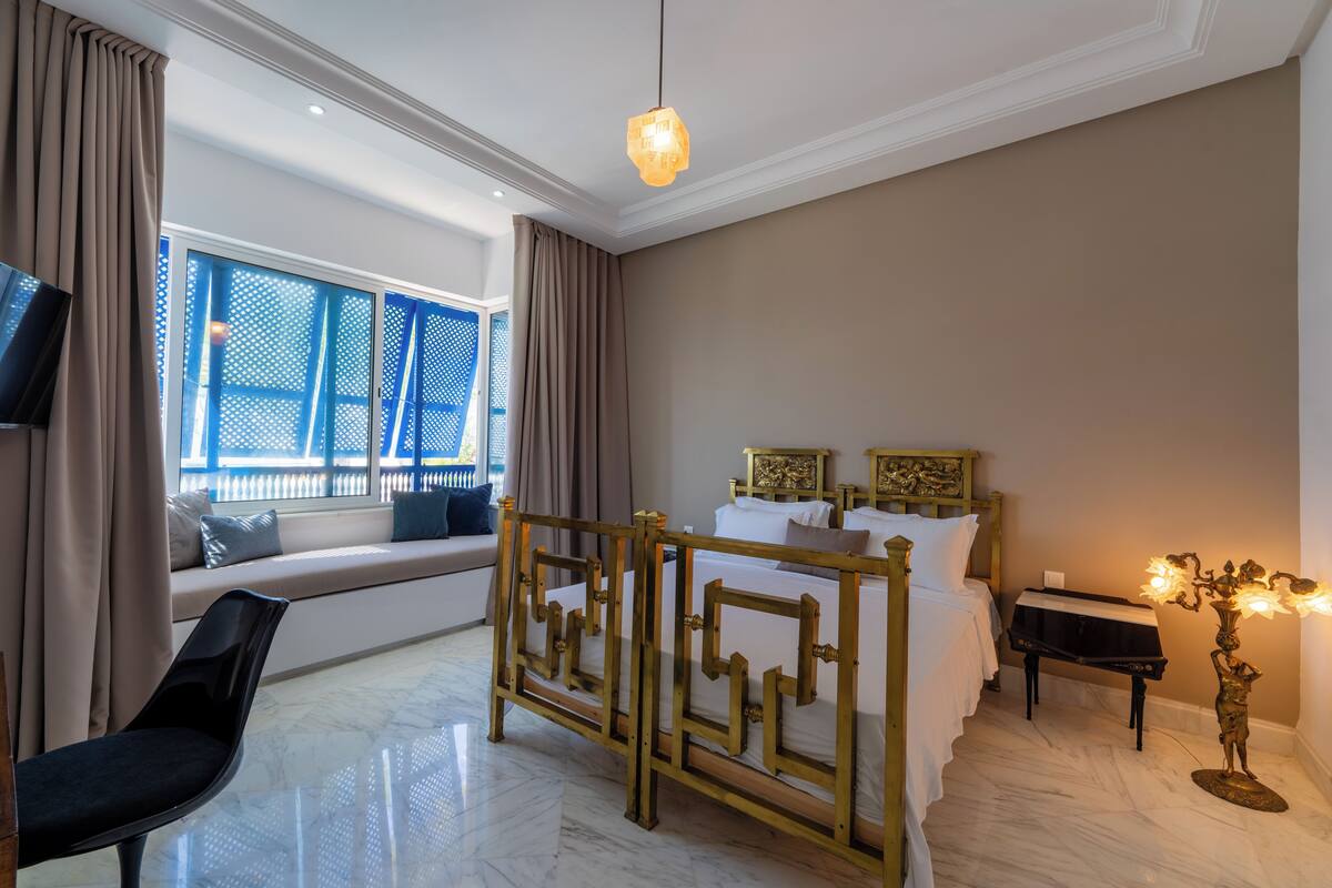 A hotel room with a bed, a piano, a TV, a chair, and a window with curtains.
