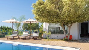 A pool area with lounge chairs and umbrellas, surrounded by trees and a building with a glass facade. - Dar Elyssa (Sidi Bou Said)