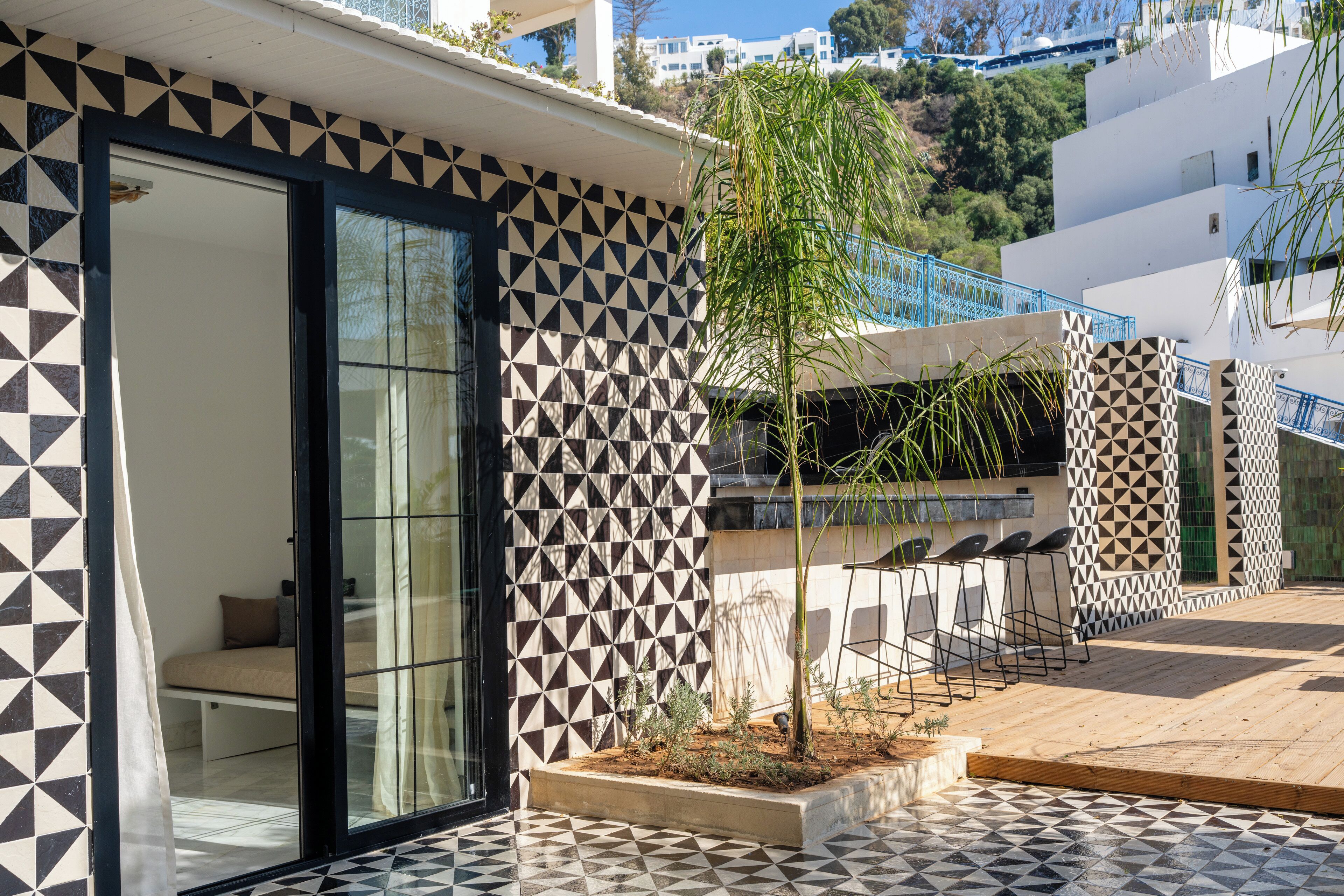 Un edificio moderno con pareti a motivi geometrici, un ingresso con porta in vetro e una piccola area esterna con un albero.