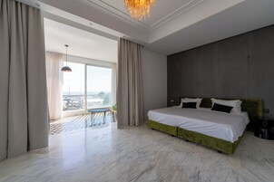 Un dormitorio amplio con una cama grande, un balcón con mesa y vistas a la ciudad.