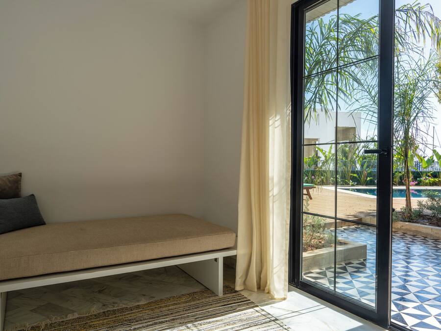Una habitación con cama, ventana con cortinas y vista al área de una piscina al aire libre.