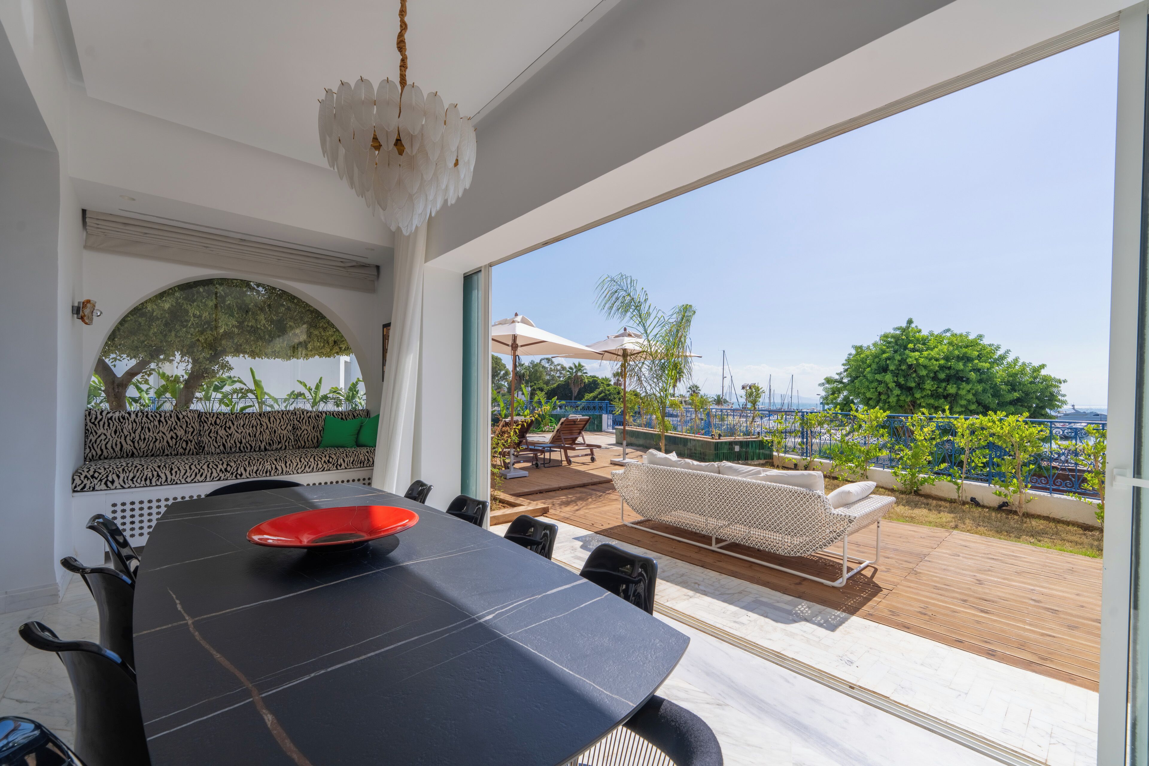 Un comedor con una mesa negra, un cuenco rojo y sillas. Se aprecia una terraza con mobiliario exterior y barandilla.