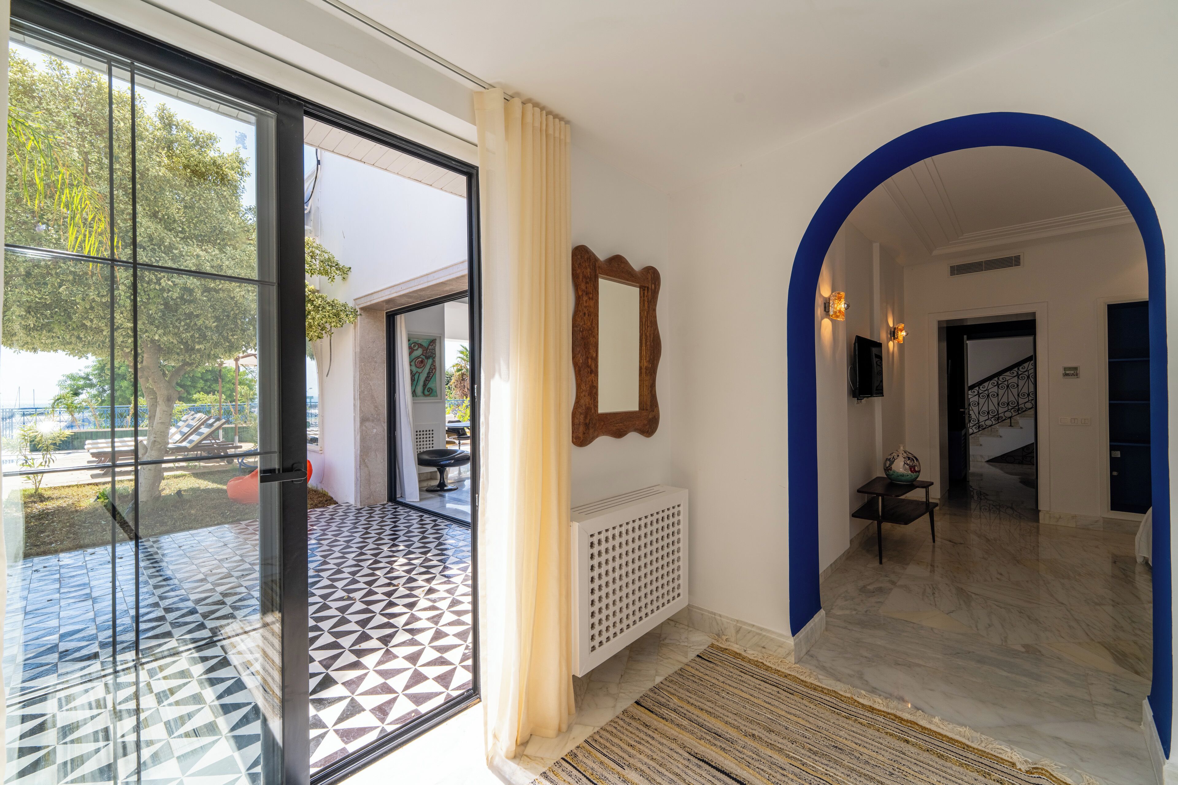 A hotel lobby with a geometric patterned floor, a large mirror, and a blue archway leading to a staircase.