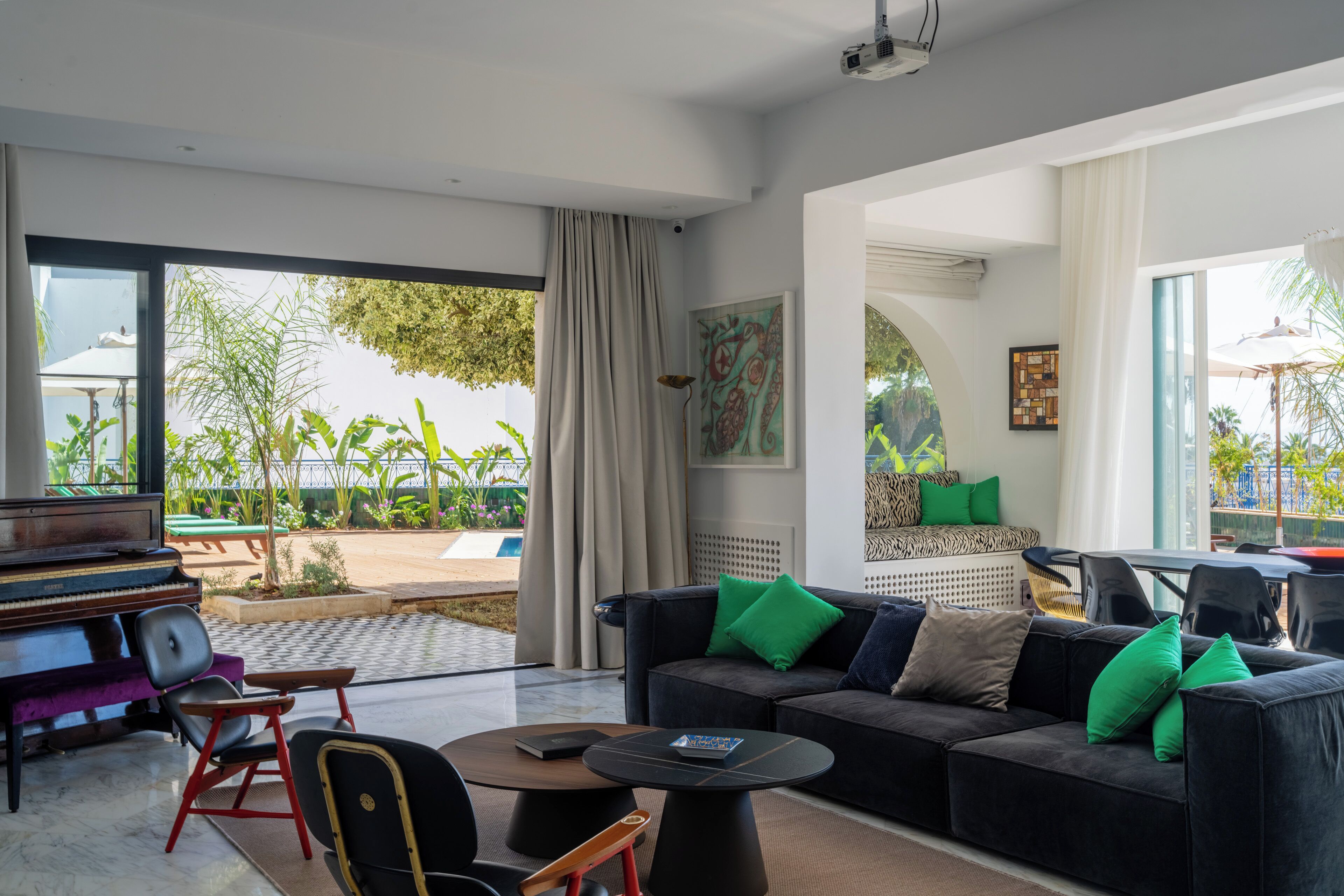 Una sala de estar moderna con un piano, un sofá con cojines verdes, una mesa de centro y vistas al área exterior.