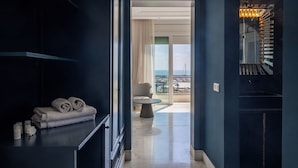 A modern hotel room with a dark blue wall, a neatly folded towel on a black shelf, a small table, and a view of the sea through a large window. - Dar Elyssa (Sidi Bou Said)