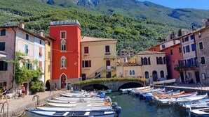 A canal with boats docked, surrounded by colorful buildings and a mountain backdrop. - 🏡 Panoramic House in Cassone - Renovated Apartment with Lake View (Malcesine)