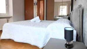 A neatly made bed with a white duvet, a bedside lamp, and a wooden door in the background. - 🏡 Panoramic House in Cassone - Renovated Apartment with Lake View (Malcesine)