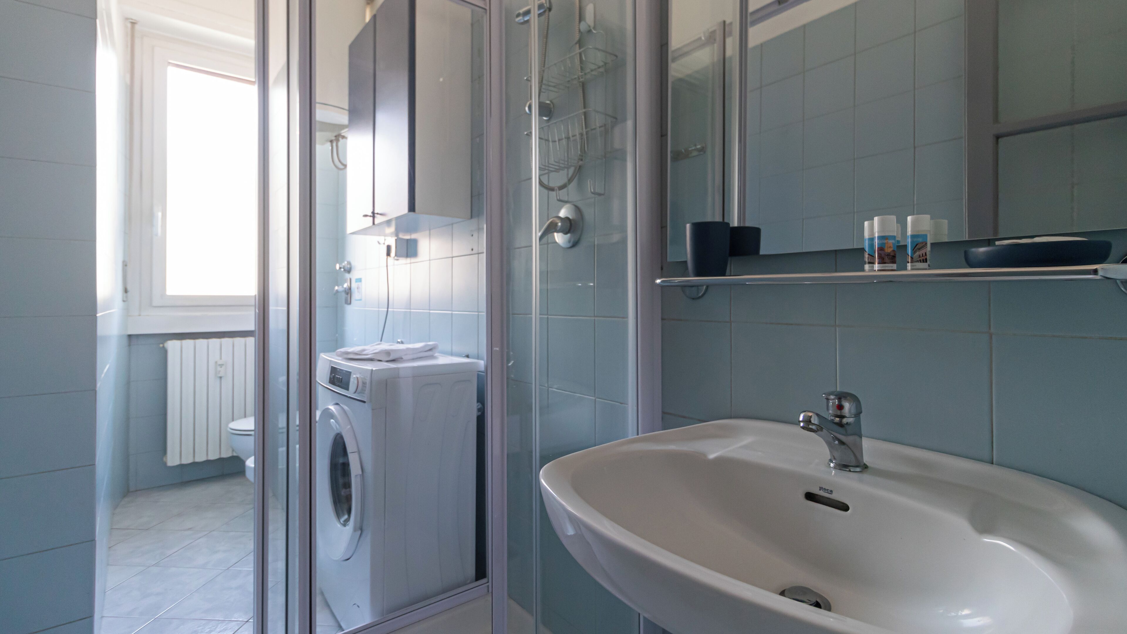 A modern bathroom with a glass shower enclosure, a washing machine, and a sink with a mirror above.