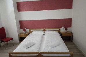 A double bed with white linens, two bedside tables with lamps, and a red chair. - The Essence of Apartment No. 1—Relaxation and Comfort in the Heart of Malcesine (Malcesine)
