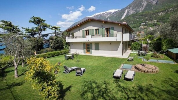 Een twee verdiepingen tellend huis met een balkon, een verzorgd gazon en een bergachtige achtergrond.