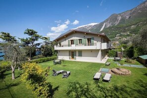 A two-story house with a balcony, a well-maintained lawn, and a mountainous backdrop. - The Essence of Apartment No. 1—Relaxation and Comfort in the Heart of Malcesine (Malcesine)