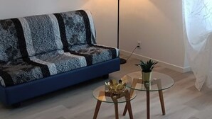 Een moderne woonkamer met een blauwe bank, een glazen salontafel met een gouden decoratief object, en een vloerlamp.