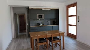Een moderne keuken met donkere kastjes, een magnetron en een eettafel met stoelen.