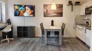 A modern kitchen with a dining area, a TV mounted on the wall, and a hanging light fixture. - Guest apartment and service apartment Hermsdorf (Hohe Börde)