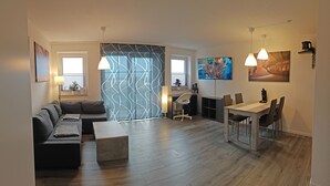 A modern living room with a sofa, coffee table, and dining area with chairs and a table. - Guest apartment and service apartment Hermsdorf (Hohe Börde)