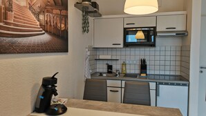 A modern kitchen with white cabinets, a microwave, and a sink. There is a dining table with chairs and a coffee machine. - Guest apartment and service apartment Hermsdorf (Hohe Börde)