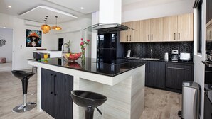 A modern kitchen with a central island, black cabinets, and a black countertop. - Modern 5 Bedrooms Pool Villa Curtis (Rawai)