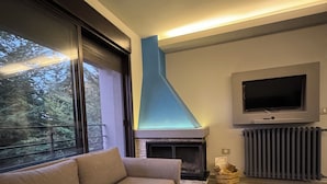 Una sala de estar moderna con sofá, chimenea, televisor y ventana con vista a árboles.