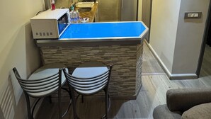 Una cocina compacta con encimera azul, dos taburetes de bar, un refrigerador y un microondas.