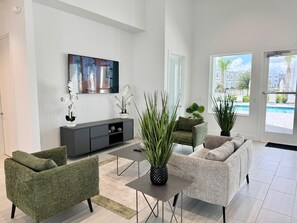 Ein modernes Wohnzimmer mit einem grauen Sofa, einem grünen Sessel, einem Couchtisch und einem großen Fenster mit Blick auf einen Pool.