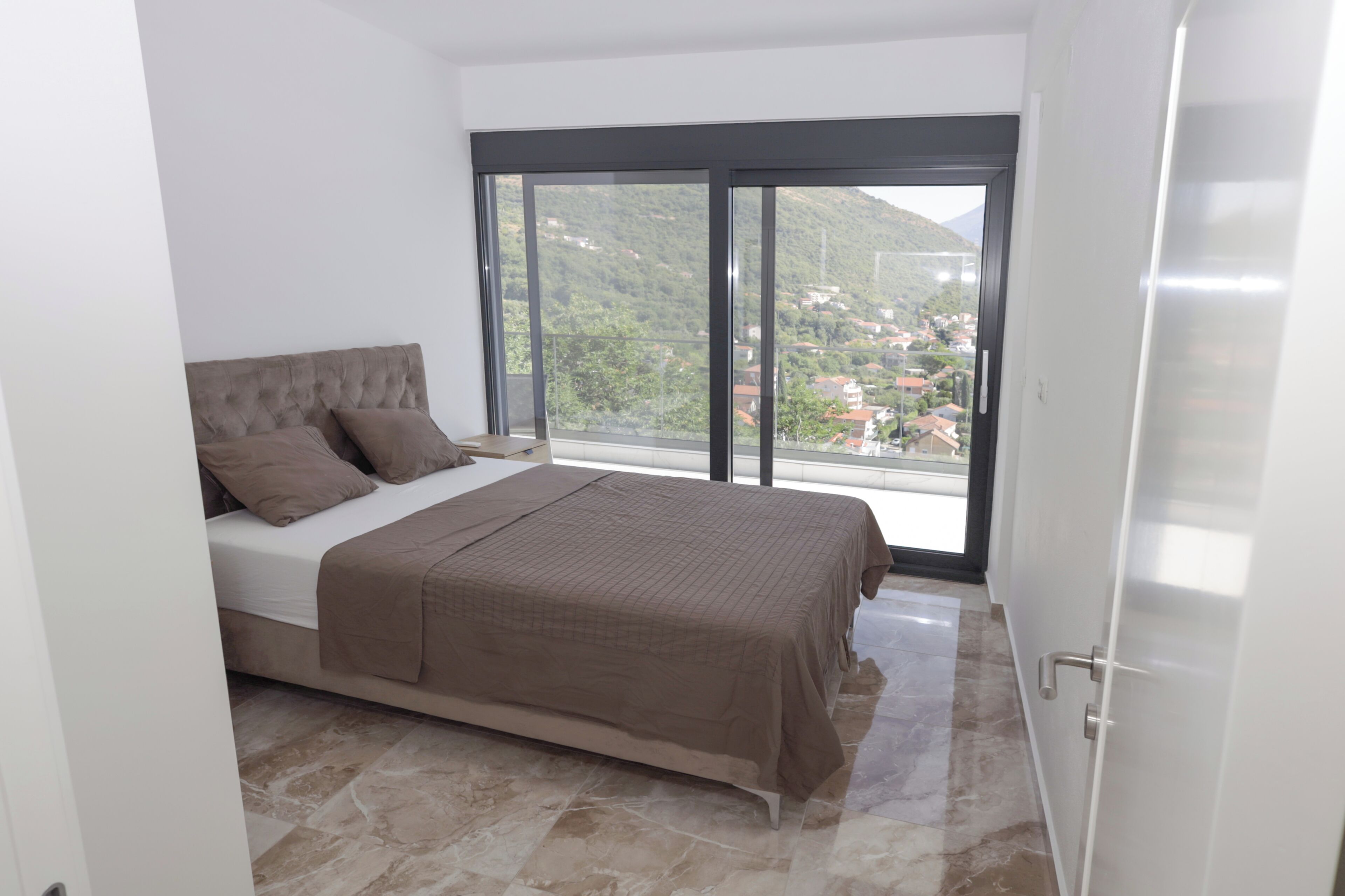 A bedroom with a bed, a view of a mountainous area, and a sliding glass door.