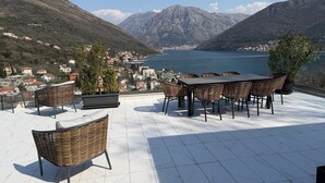 A terrace with a table and chairs, potted plants, and a view of a lake and mountains. - The house is our passion project, built with love surrounded by forest and views (Kamenari)