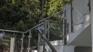 A staircase with glass railings leading to a covered area with trees in the background. - The house is our passion project, built with love surrounded by forest and views (Kamenari)