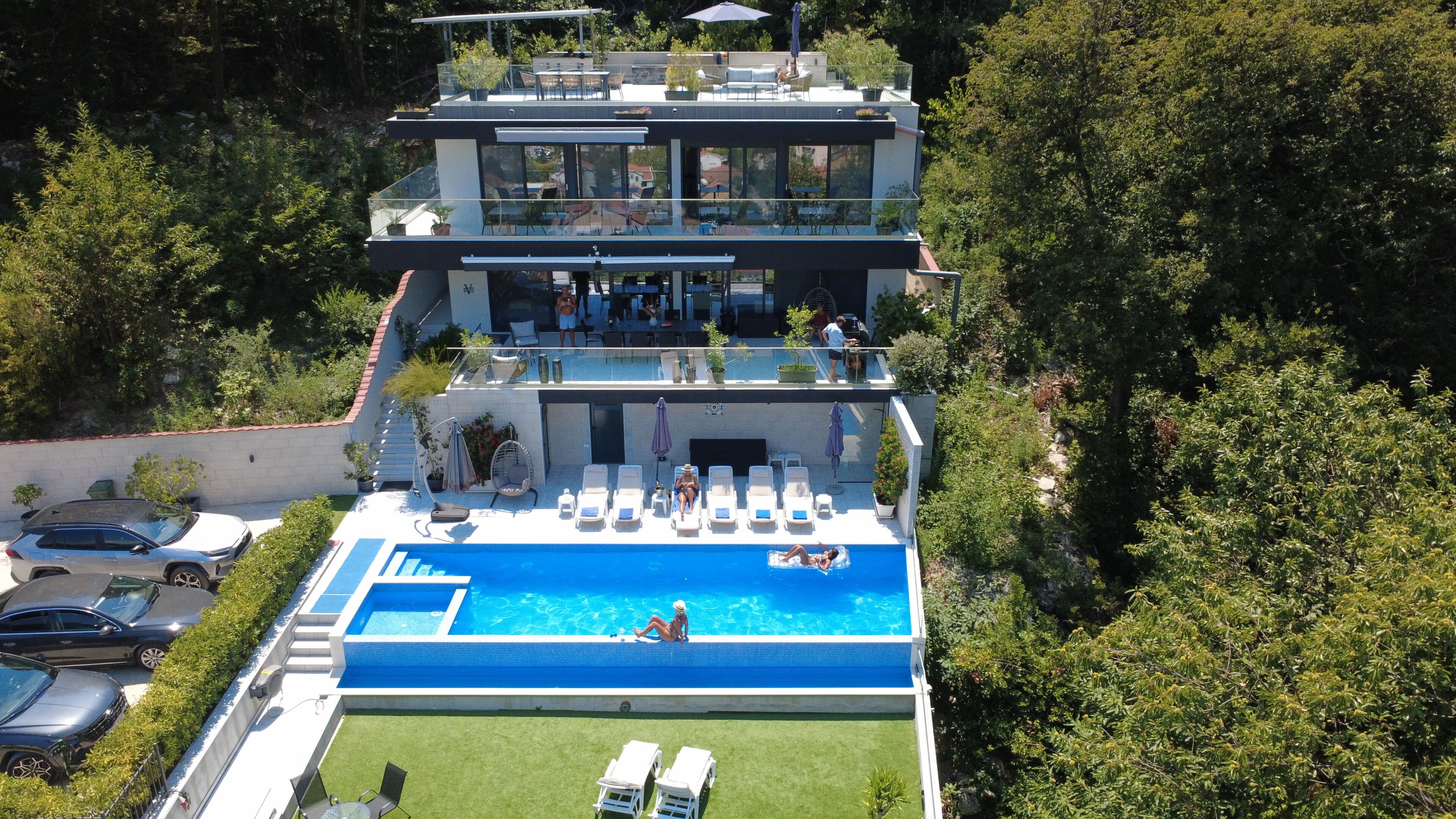 A modern multi-story building with a rooftop terrace, a swimming pool, and a well-maintained lawn.