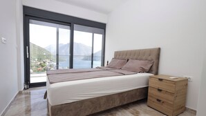 A bedroom with a bed, a nightstand, and a large window offering a view of a mountainous landscape. - The house is our passion project, built with love surrounded by forest and views (Kamenari)