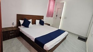 A neatly made bed with a wooden headboard, a bedside table, and a nightstand. - Ram Darshan Palace (Tarabganj)