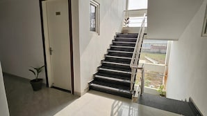 A staircase with a handrail leading to an upper floor, a door with a number sign, and a potted plant on the floor. - Ram Darshan Palace (Tarabganj)