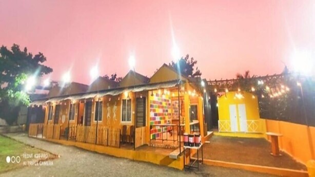 A row of brightly lit, colorful cabins with a small outdoor seating area and a yellow building in the background. - Mandav Hills Resort (Dhar)