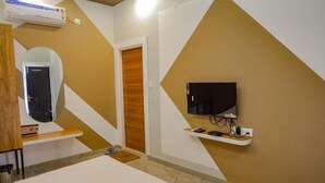 A hotel room with a bed, a TV mounted on the wall, a wooden door, and an air conditioning unit. - Mandav Hills Resort (Dhar)