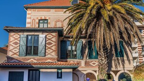 A two-story building with a tiled roof, a palm tree in front, and a paved driveway. - Apartment Arcachon Centre "Escale sur le Bassin" (Stopover on the Basin) (ARCACHON)