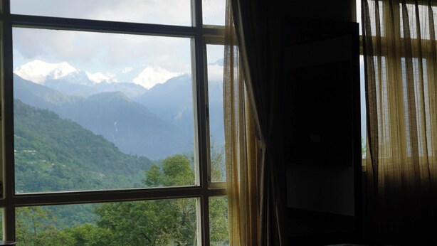 Una habitación con un ventanal que ofrece vistas a montañas nevadas y colinas verdes exuberantes.